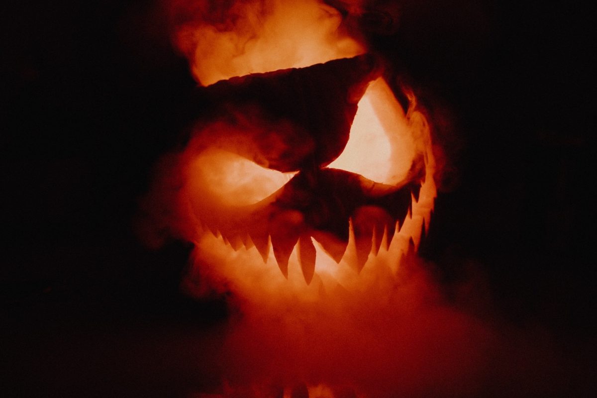 Gruseliger Halloween-Kürbis mit leuchtenden Augen und Mund in dunkler Umgebung.