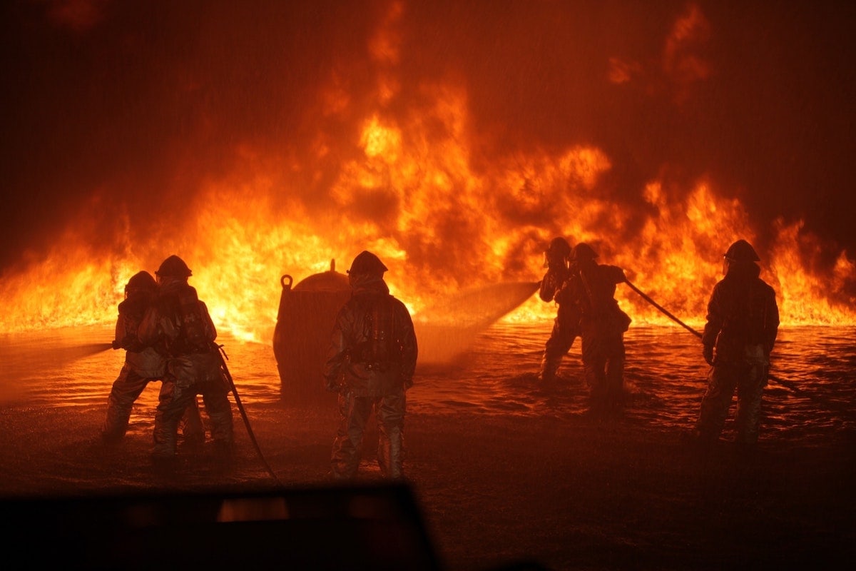 Feuerwehrleute löschen einen großen Brand mit Wasser in dunkler Umgebung.
