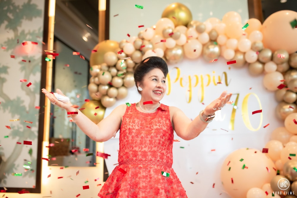 Poppin raises her arms as confetti falls at her 70th birthday party in Bangkok