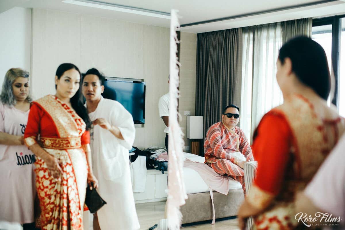 The Nepali bride in a red and gold sari gets ready with her bridesmaids in a hotel suite in Pattaya