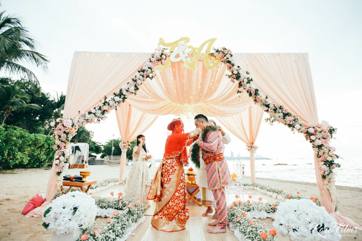 Bride and groom exchange flower garlands under the floral mandap on the beach at Cape Dara Resort, Pattaya