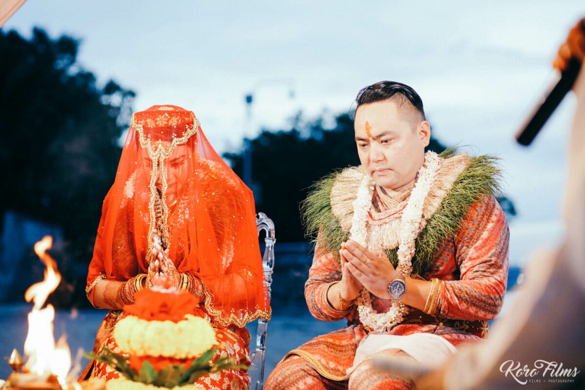 Veiled Nepali bride in red and the groom in garlands pray beside the sacred fire at their beach ceremony at Cape Dara Resort, Pattaya