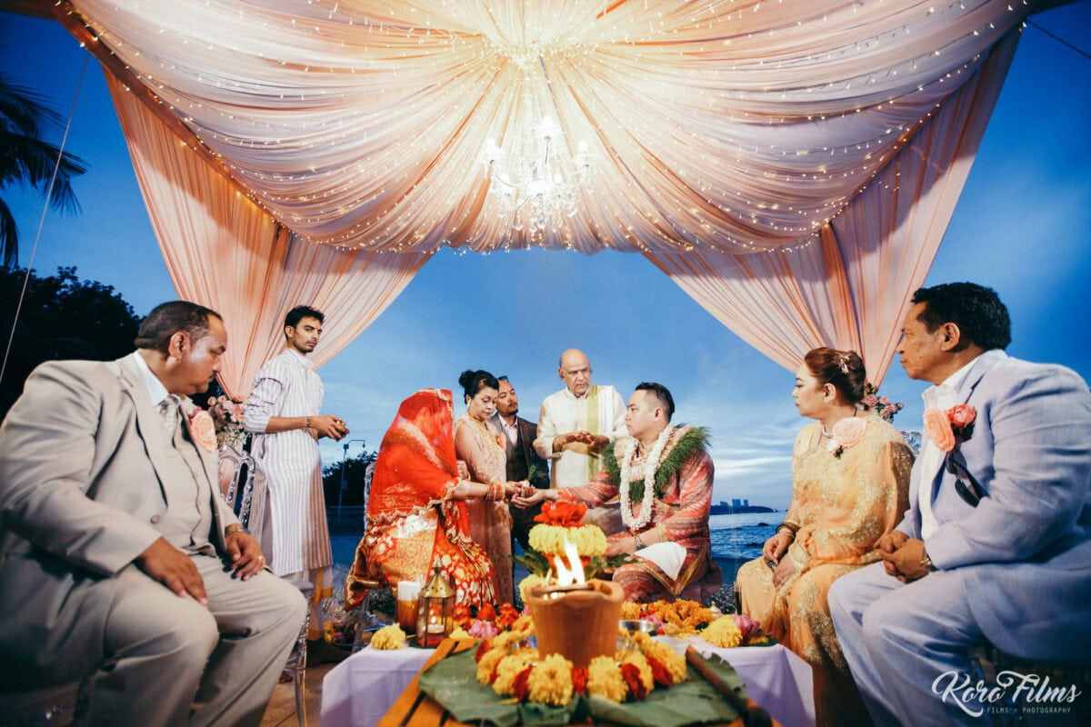 The couple and their families sit around the sacred fire under the mandap at blue hour, Cape Dara Resort, Pattaya
