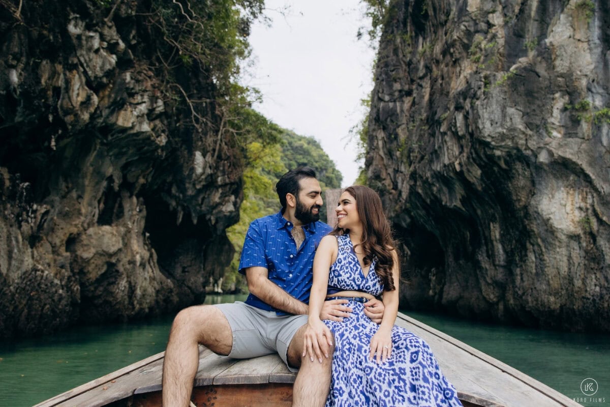 Jyotika and Neel sit on the bow of a long-tail boat between limestone cliffs in the Ko Hong lagoon, Krabi