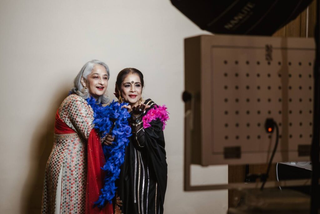 Two guests with a feather boa pose in front of a white backdrop, shown in black and white