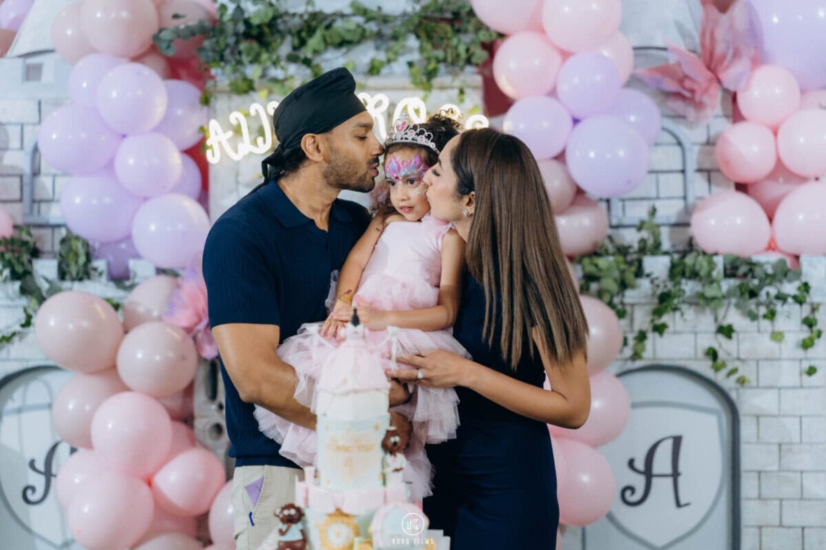 Parents kiss their daughter Alina Rose in front of a pink balloon wall at her 4th birthday party at Hotel Lotus Sukhumvit 33, Bangkok