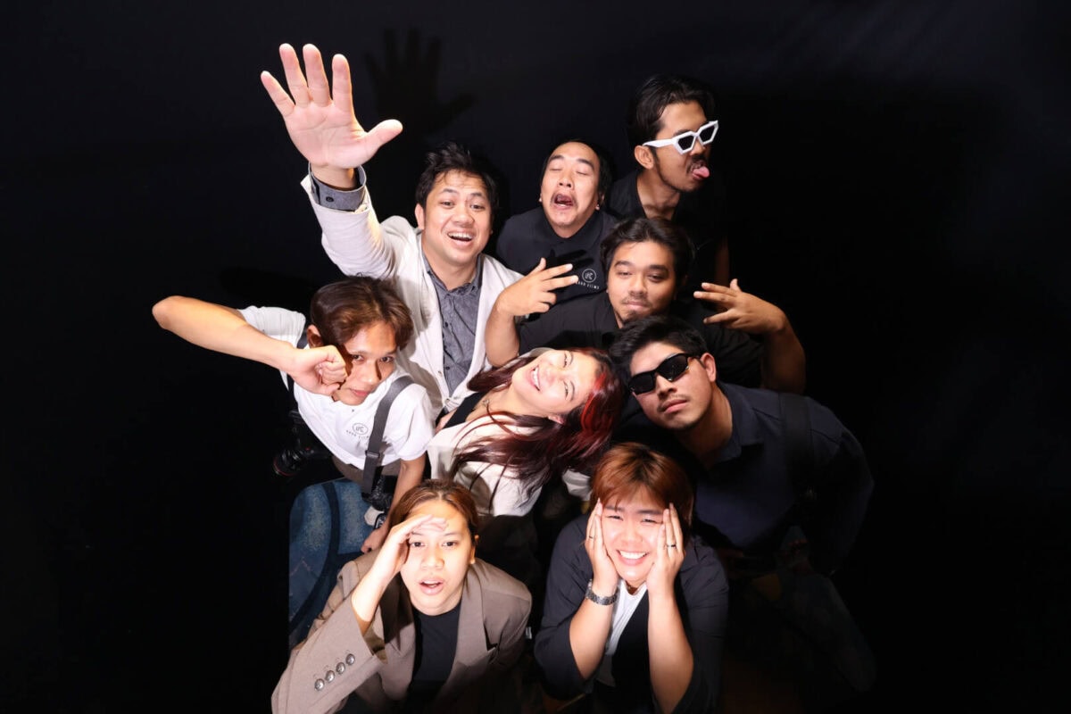Top view photo booth group photo: nine guests pose and wave up at the overhead camera on a black backdrop