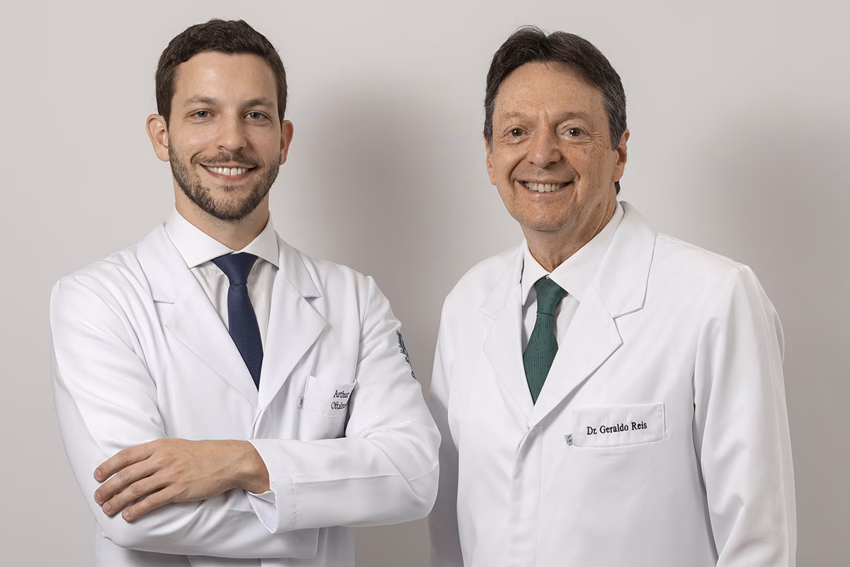 Dois oftalmologistas, pai e filho, de jaleco no consultório