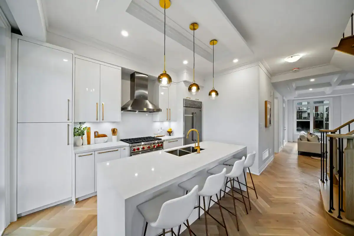 Modern luxury kitchen at Fifth Avenue Homes Woodbridge with white cabinetry, a large waterfall island, gold hardware, and high-end stainless steel appliances.