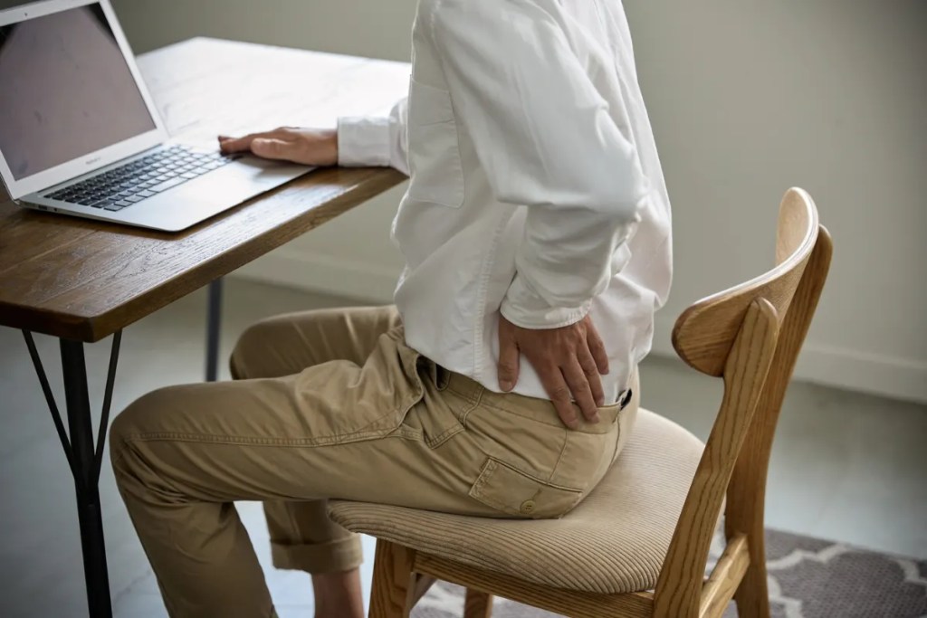 Man holding lower back pain home Man experiencing symptoms of either a pilonidal cyst or perianal abscess