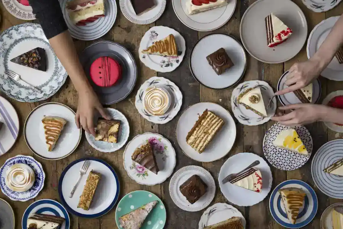 assortment of Prestige Patisserie handmade cakes on vintage plates – sliced cakes, pastries and desserts arranged on a rustic wooden table