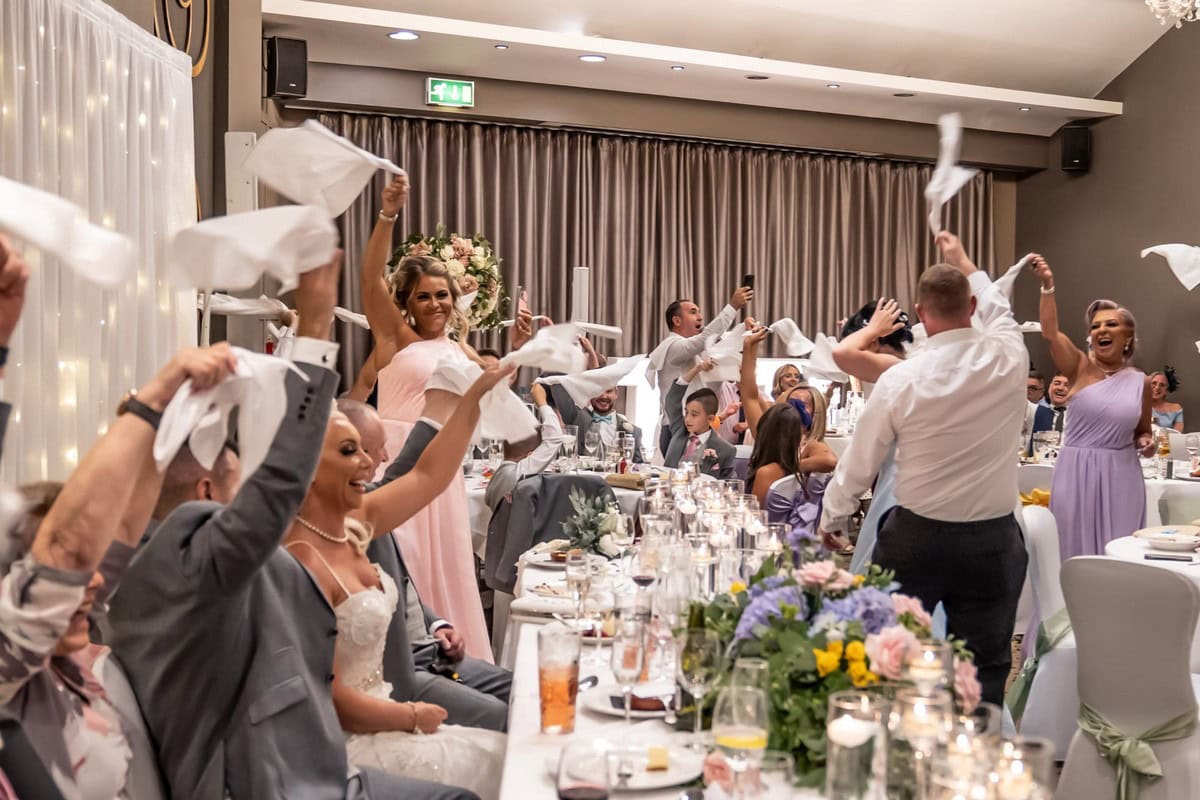 Wedding guests participating in a signature napkin-waving moment during The Sing Along Waiters performance at Red Hall Hotel, showing bride and wedding party fully engaged in the entertainment