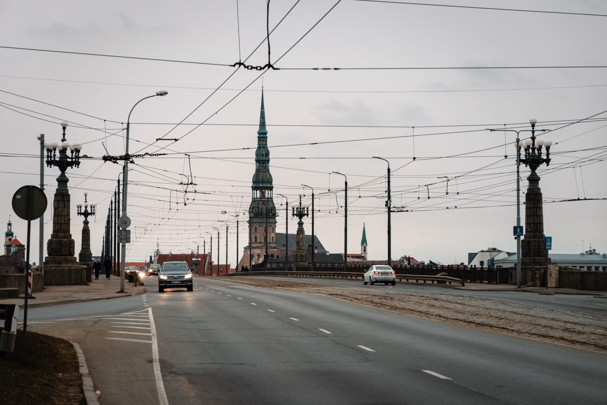 Empty roadway leading into Riga, Latvia with overhead tram wires and church spires in the distance