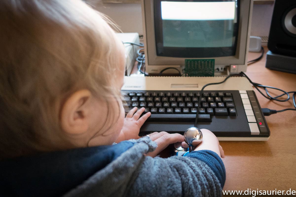 Kleinkind sitzt an einem alten 8-Bit-Computer und drückt einen Joystick-Knopf