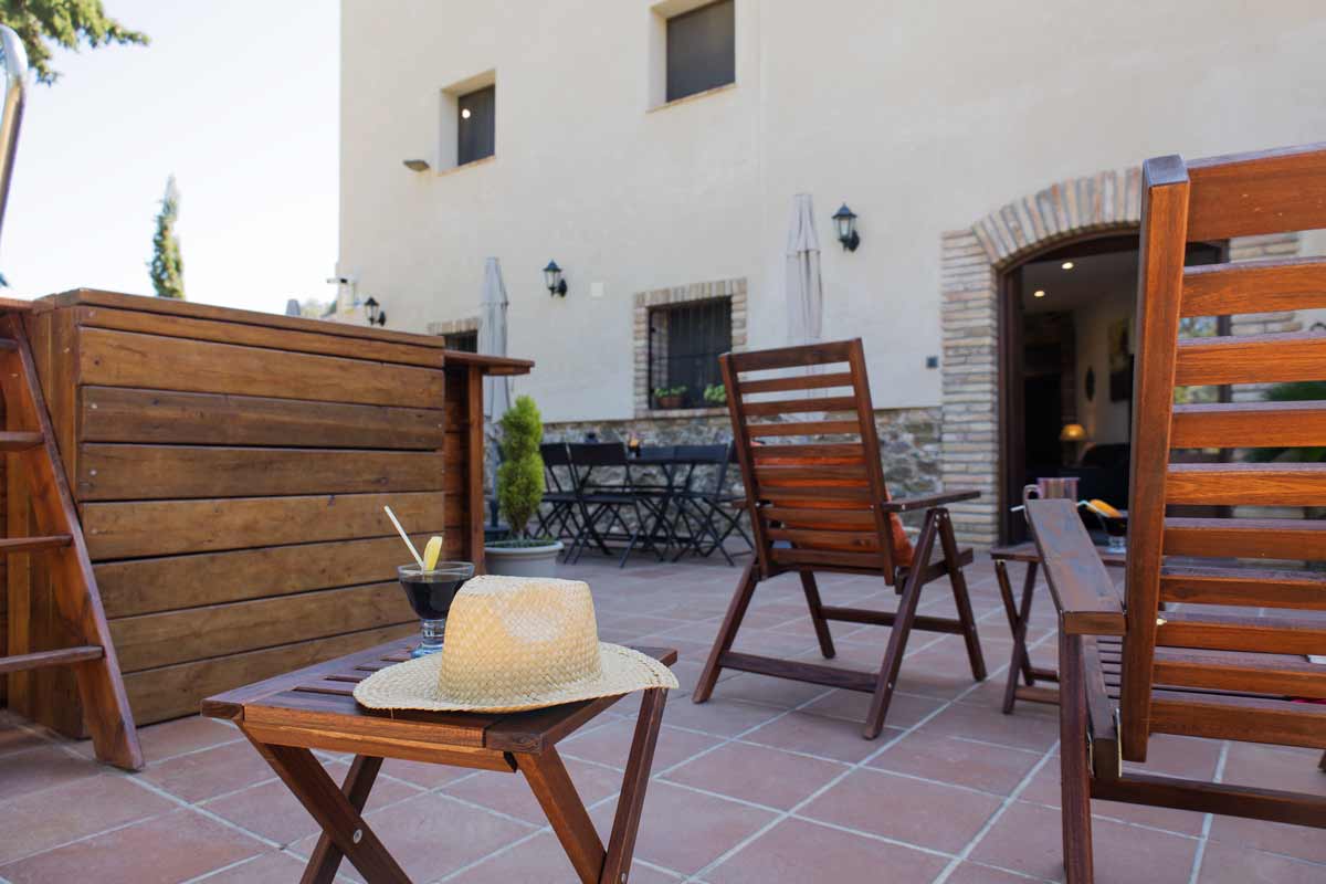 Terraza donde hay una piscina, unas hamacas de madera y mesas y sillas con parasoles.