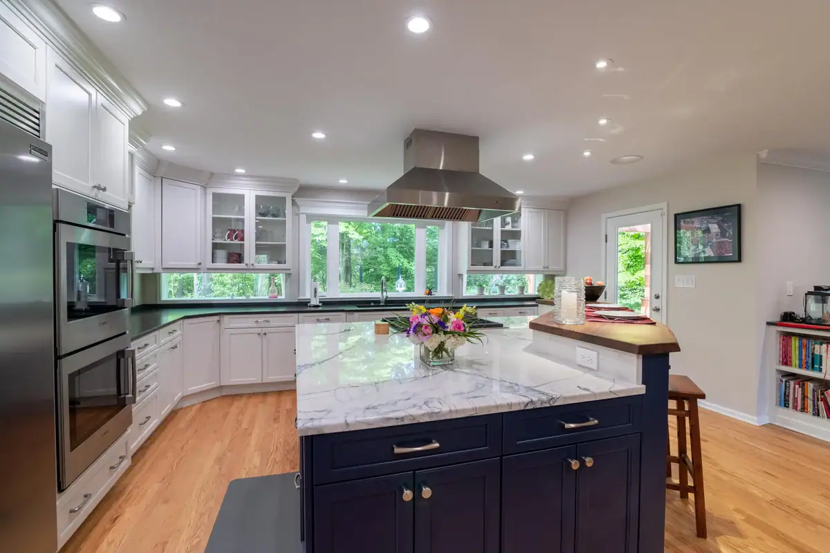 Bright kitchen with white upper cabinets, a dark blue island topped with white marble, and hardwood floors.