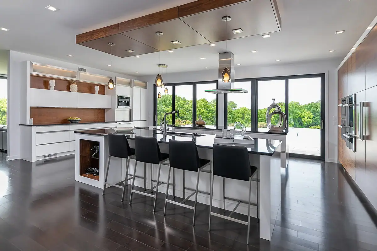 Modern, luxury kitchen with a large black island, high-gloss white and wood cabinetry, and large windows overlooking a green landscape.