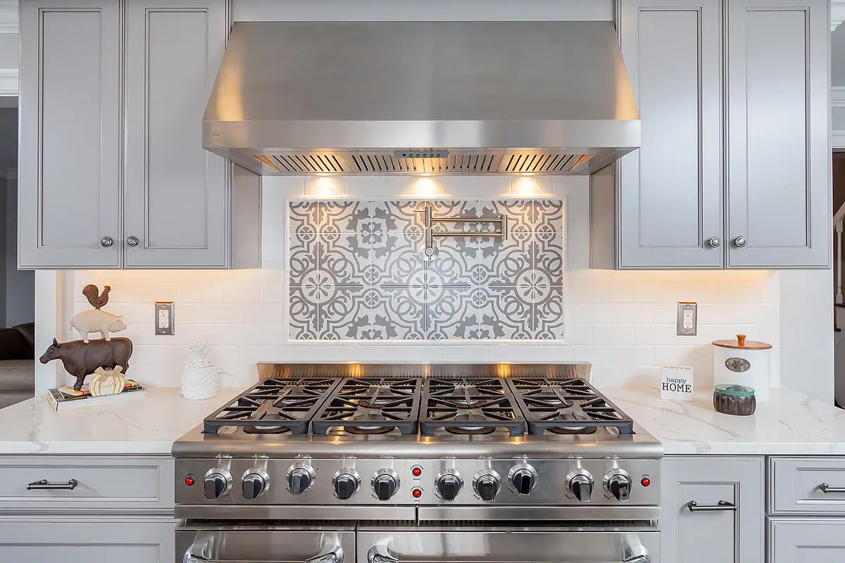 Close-up of a high-end stainless steel range under a matching hood, centered between light gray cabinets.