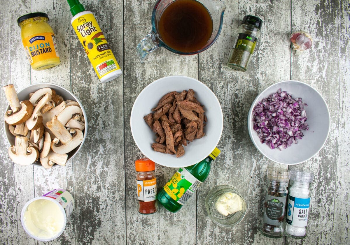 ingredients for leftover roast beef stroganoff on table. Beef, red onion, mushrooms, mustard, cooking spray, stock, parsley, garlic, salt and pepper, butter, lemon juice and paprika.