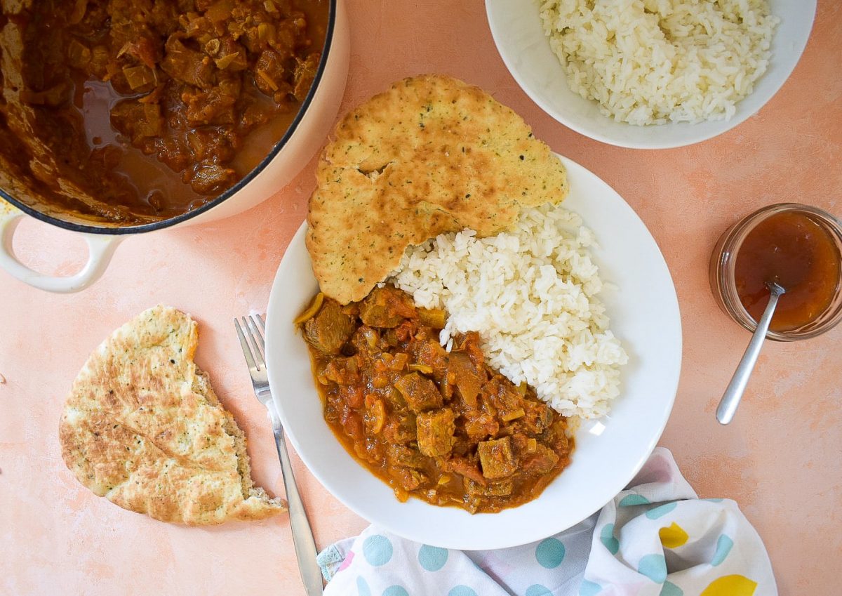 Top view of bowl of served curry with rice, surrounded by condiments and sides.