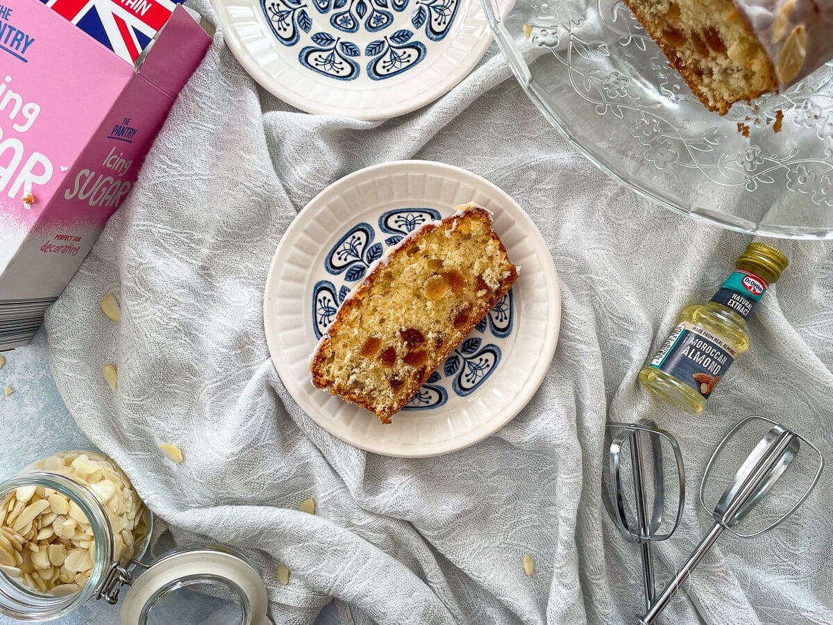 close up of slice of cherry loaf cake on small blue patterned plate.