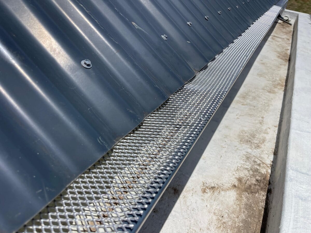 Aluminium mesh gutter guard fitted along the gutter of a dark grey corrugated roof, closing it off so birds cannot get in to roost or nest.