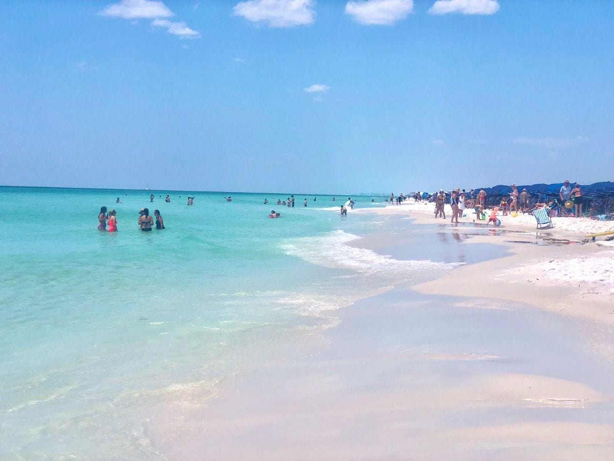 beach with people in water and blue umbrellas