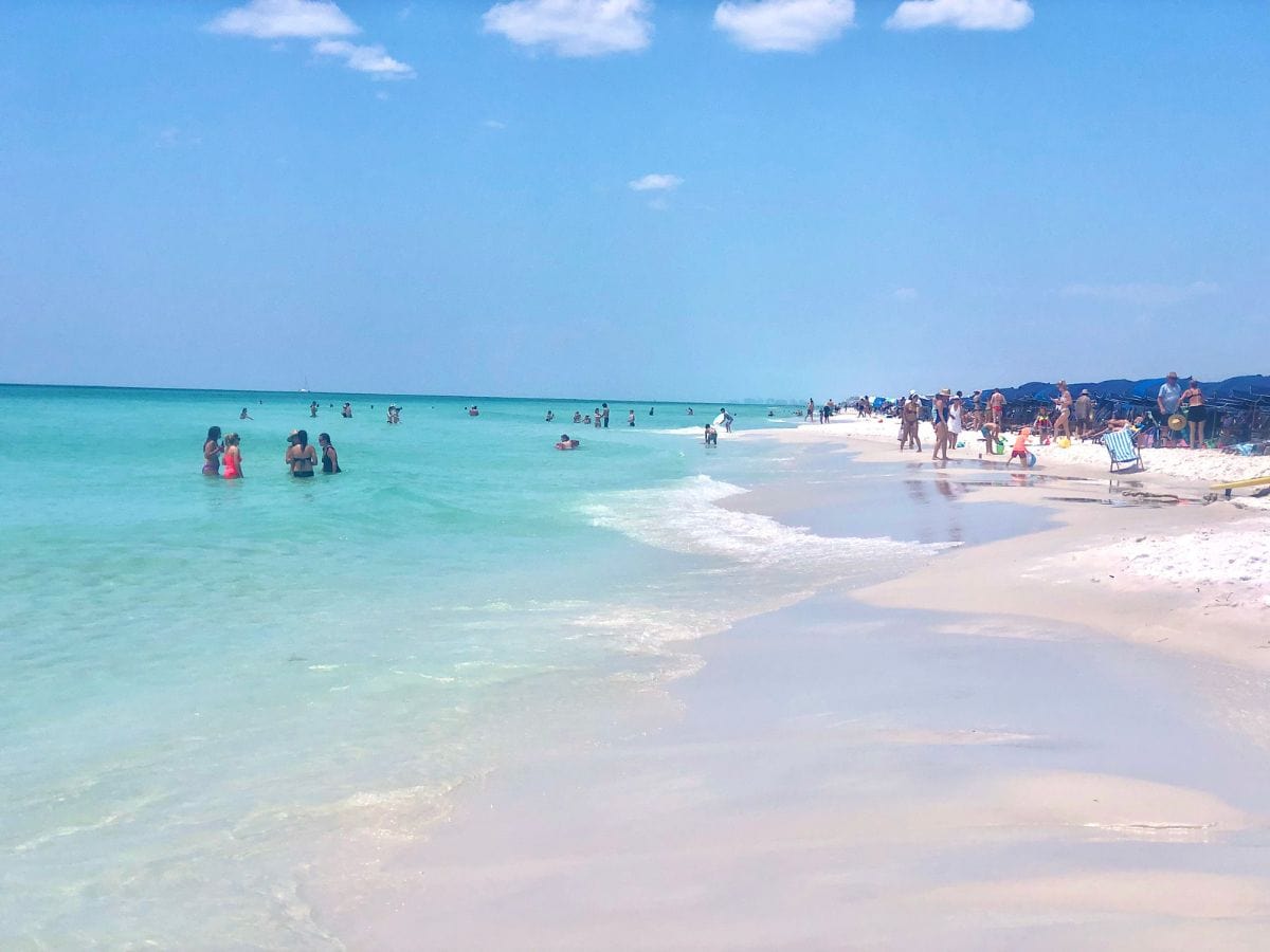 beach with people in water and blue umbrellas