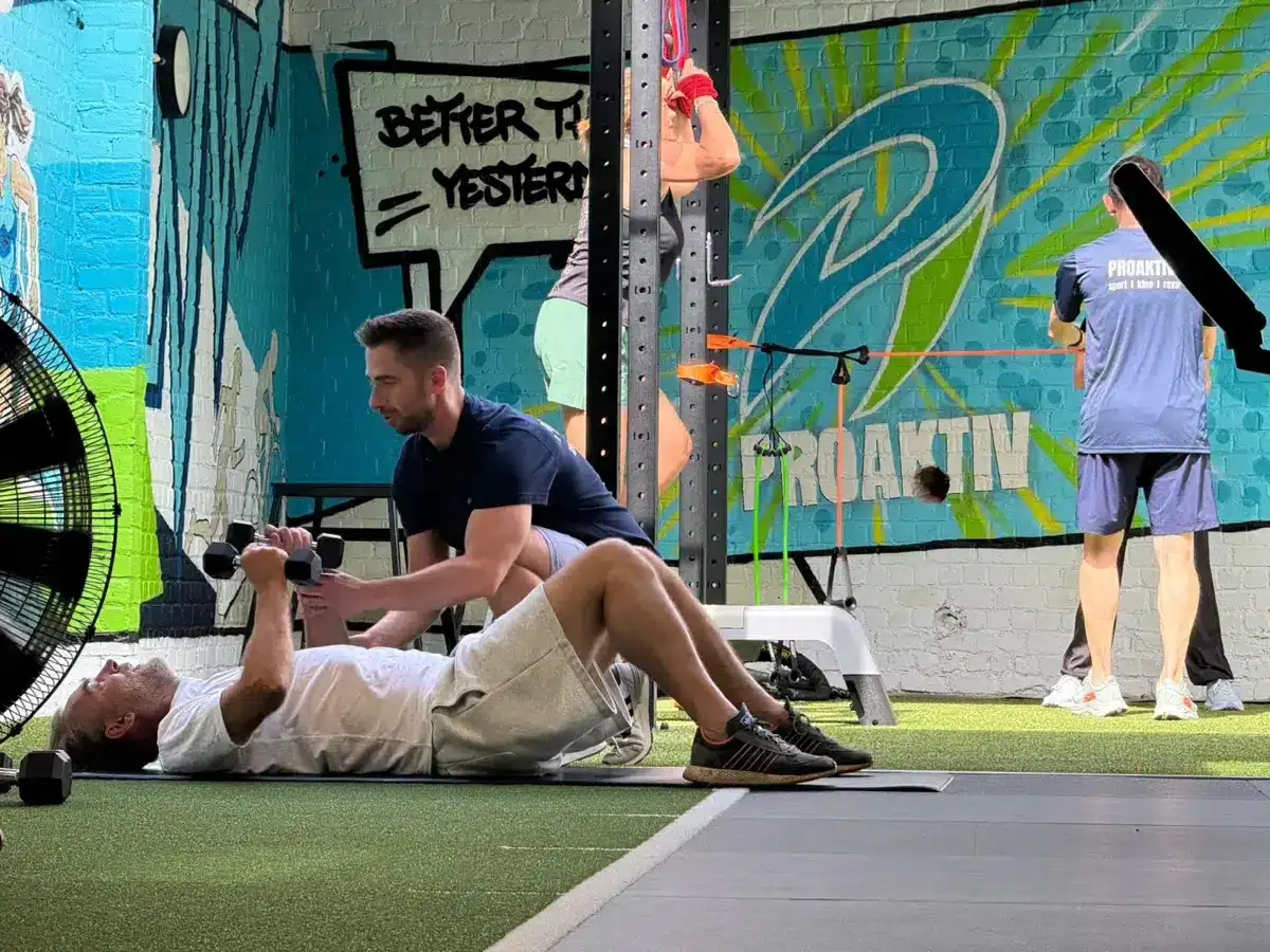 Een deelnemer voert een krachtoefening met dumbbells uit onder begeleiding tijdens een Healthy Ageing-proefles bij ProAktiv. in Haacht