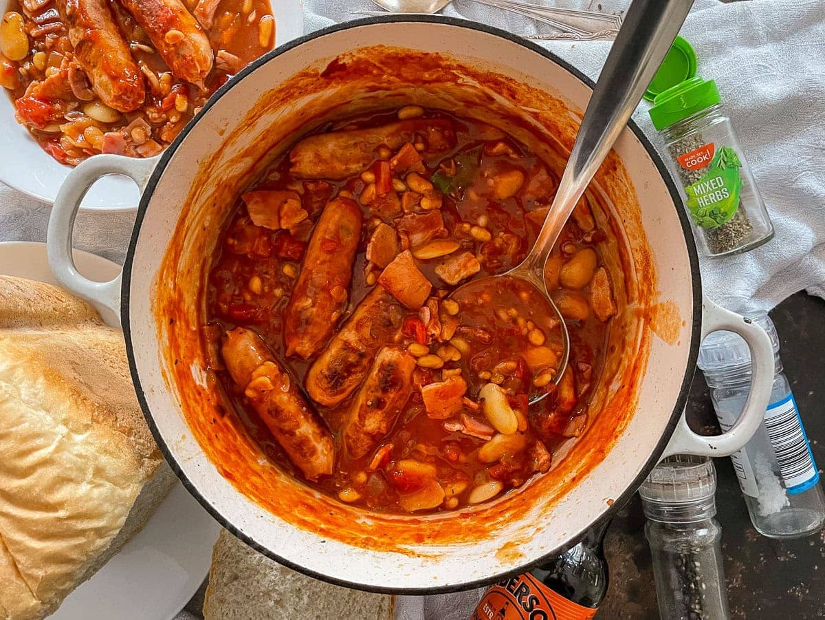 bacon, sausage and baked bean casserole in tomato sauce cooking in Dutch Oven.
