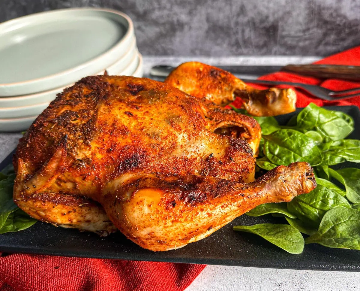 Whole Chicken slow cooked then grilled to golden brown on a black platter with spinach. 