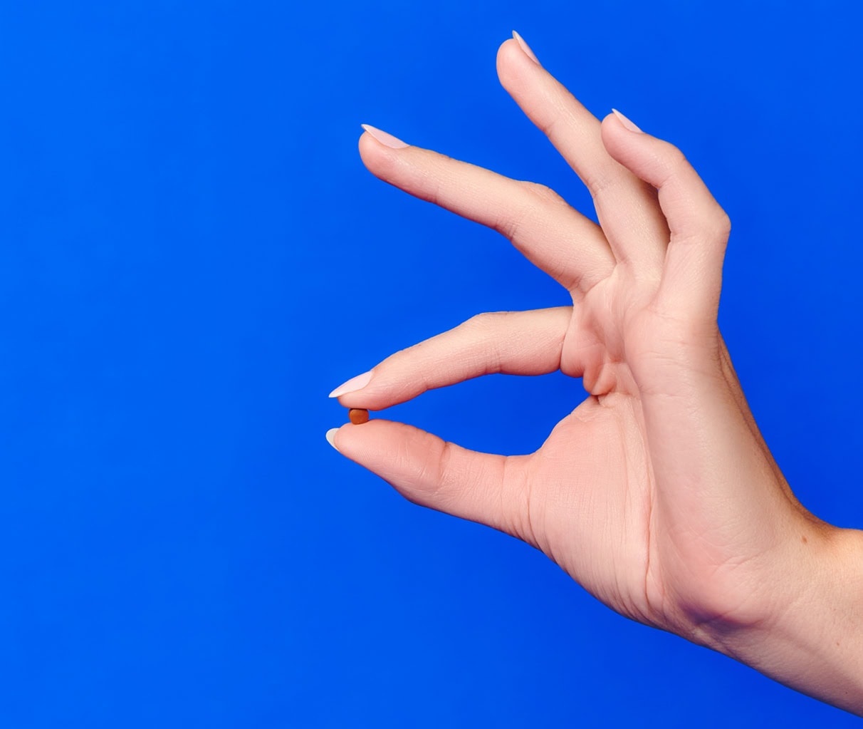 A hand making an ok sign with two fingers while holding a pill.