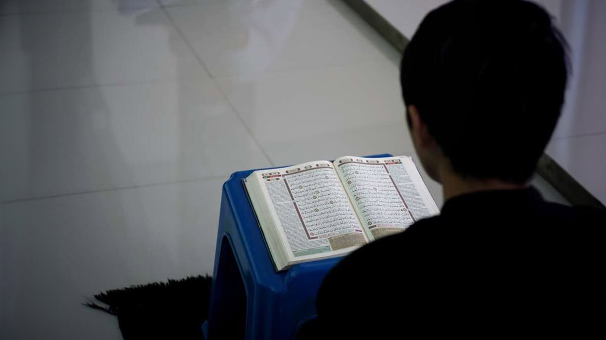 A person reading the Quran placed on a blue stand in online islamic dar class