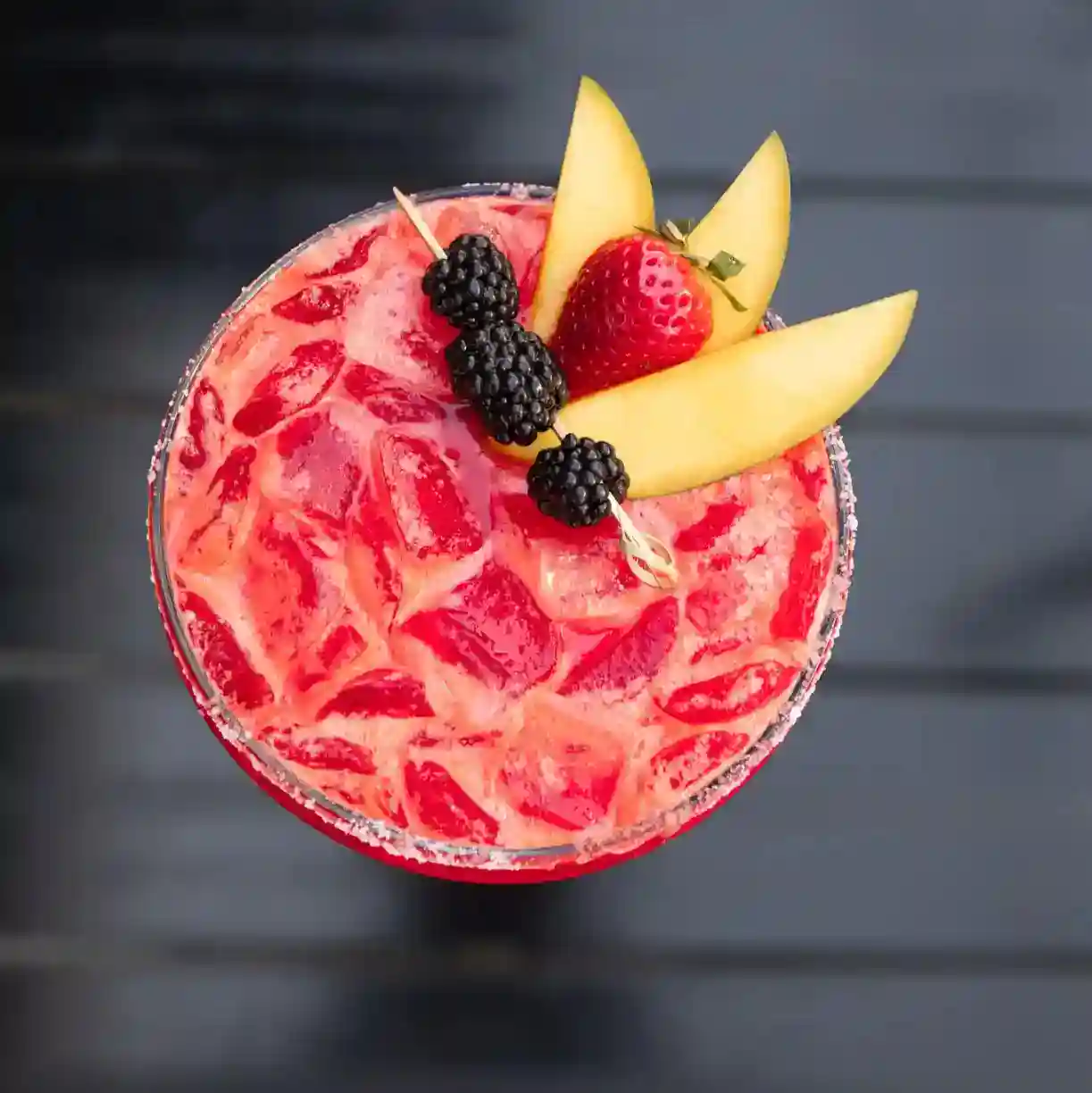 Refreshing berry and melon margarita served over ice with a sugar-rimmed glass, garnished with fresh cantaloupe slices, blackberries, and a strawberry at an upscale Raleigh Mexican restaurant