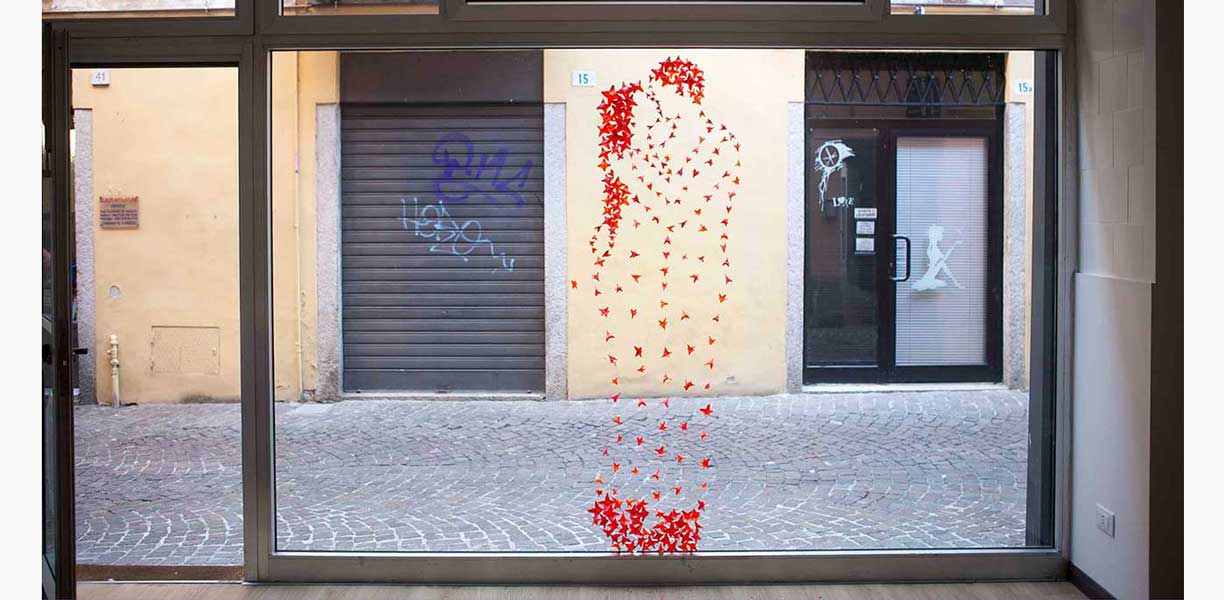 title kiss-of-spring, 2016 installation by Kazumasa Mizokami, designed by a young man and woman kissing in a red plastic bougainvillea on a windshield facing the old Bertini street.