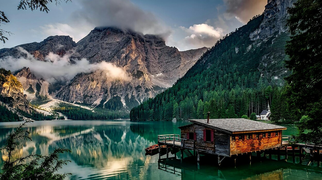 mirror lake reflecting wooden house in middle of lake overlooking mountain ranges