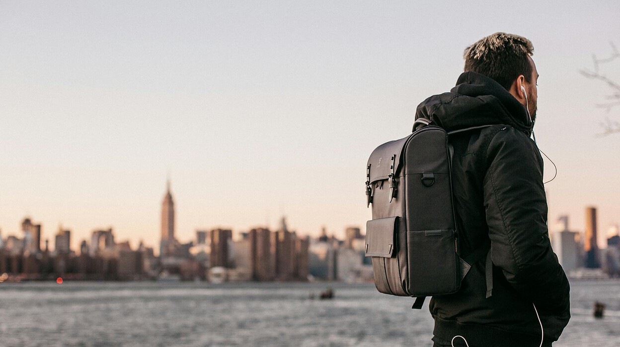 man wearing black bubble jacket and black leather backpack near bay