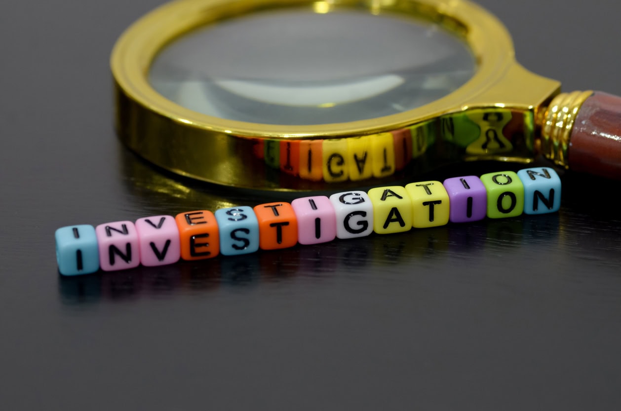 a magnifying glass placed next to a line of colorful beads spelling out the word INVESTIGATION.