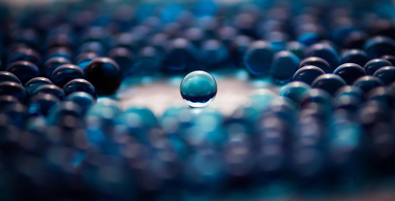 Eine glänzende blaue Glaskugel steht im Fokus, umgeben von unscharfen Kugeln – Symbol für Individualität, Fokus und maßgeschneiderte Lösungen im digitalen Zeitalter.