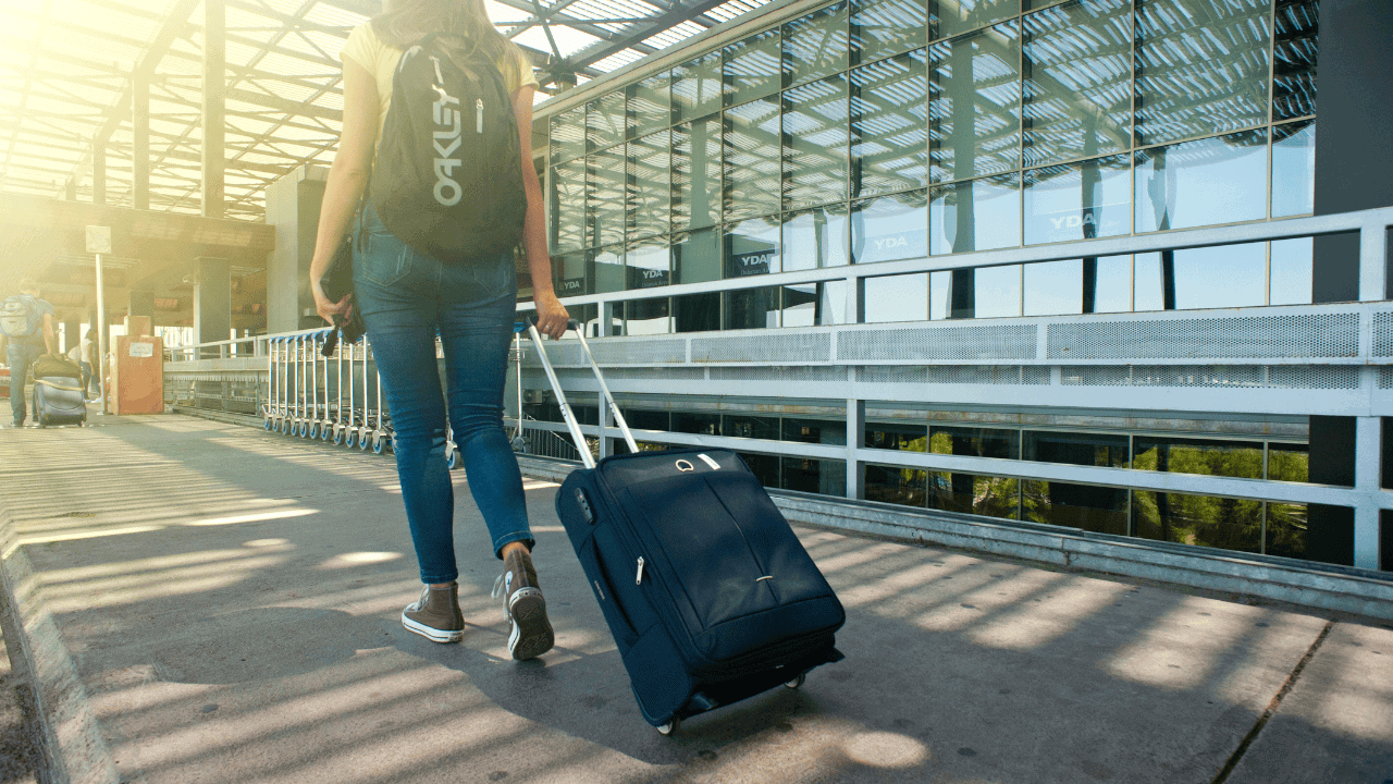 Woman with rolling suitcase at airport terminal, travel tips for a smooth vacation.