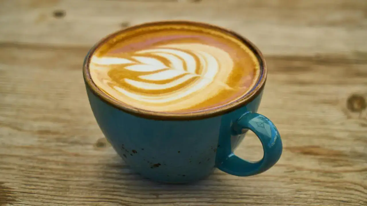 Xícara de café com leite decorado com latte art sobre mesa de madeira, típica de cafeterias em Santiago.