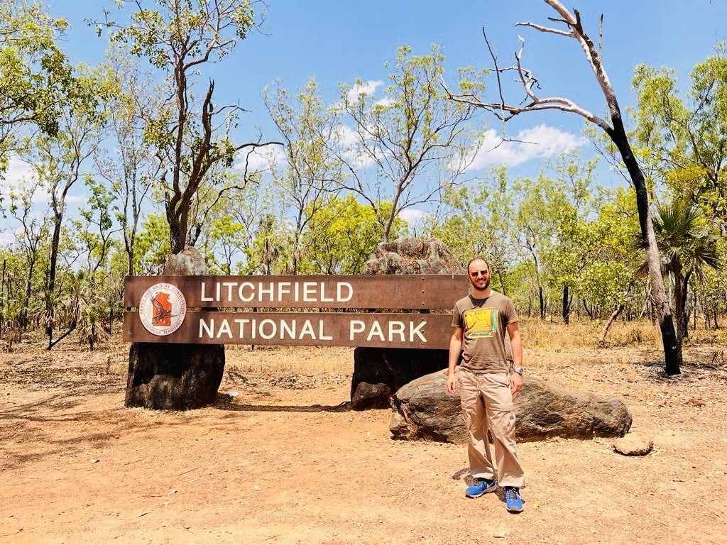 Man standing in front of Litchfield National Park entry sign in Australia, on a sunny day