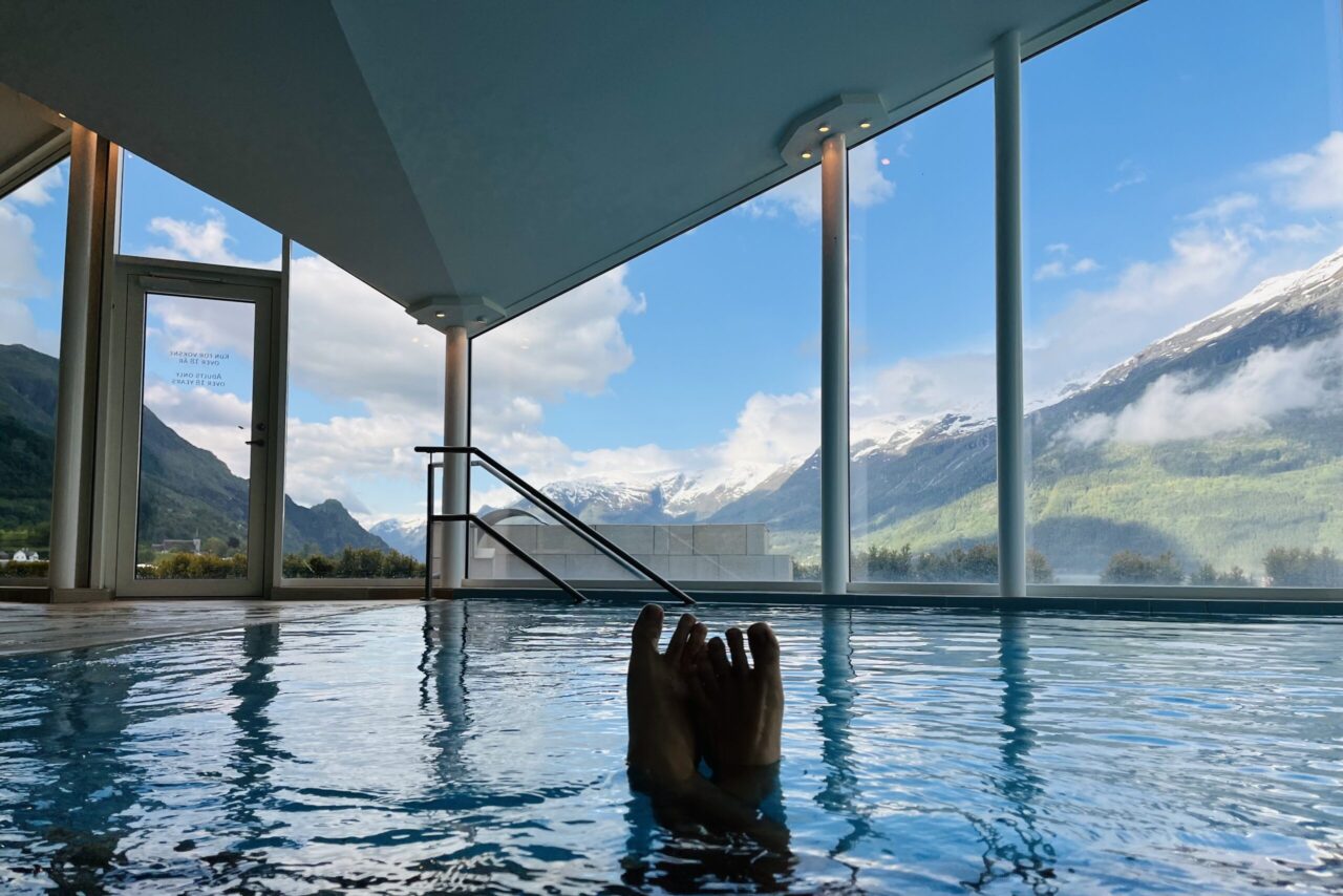 person in a indoor swimming pool with view of snowy mountains outside, on a sunny day