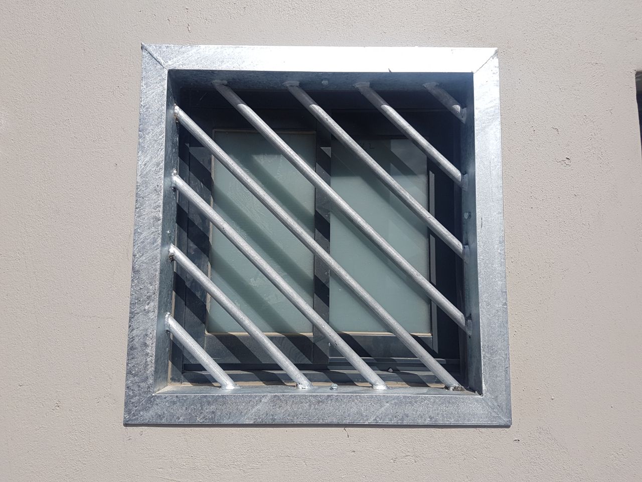 Custom galvanised steel diagonal bars in a square frame on a small window—robust, modern window burglar bars designs for exterior security.