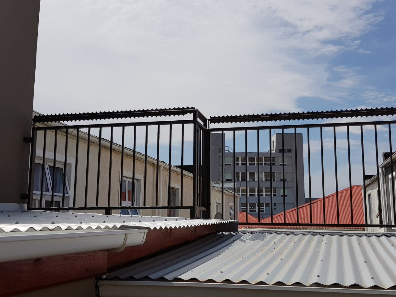 Dark rotating security spikes intalled on the fence of an urban rooftop in Cape Town, set against the backdrop of city buildings.