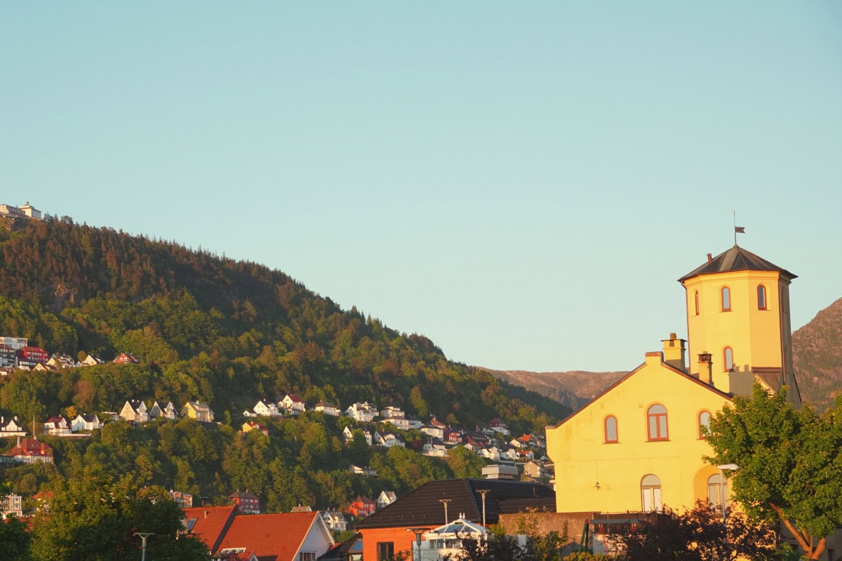 nordnes_peninsula_sunny_day_bergen Yellow building with a background of mountains and houses in Bergen