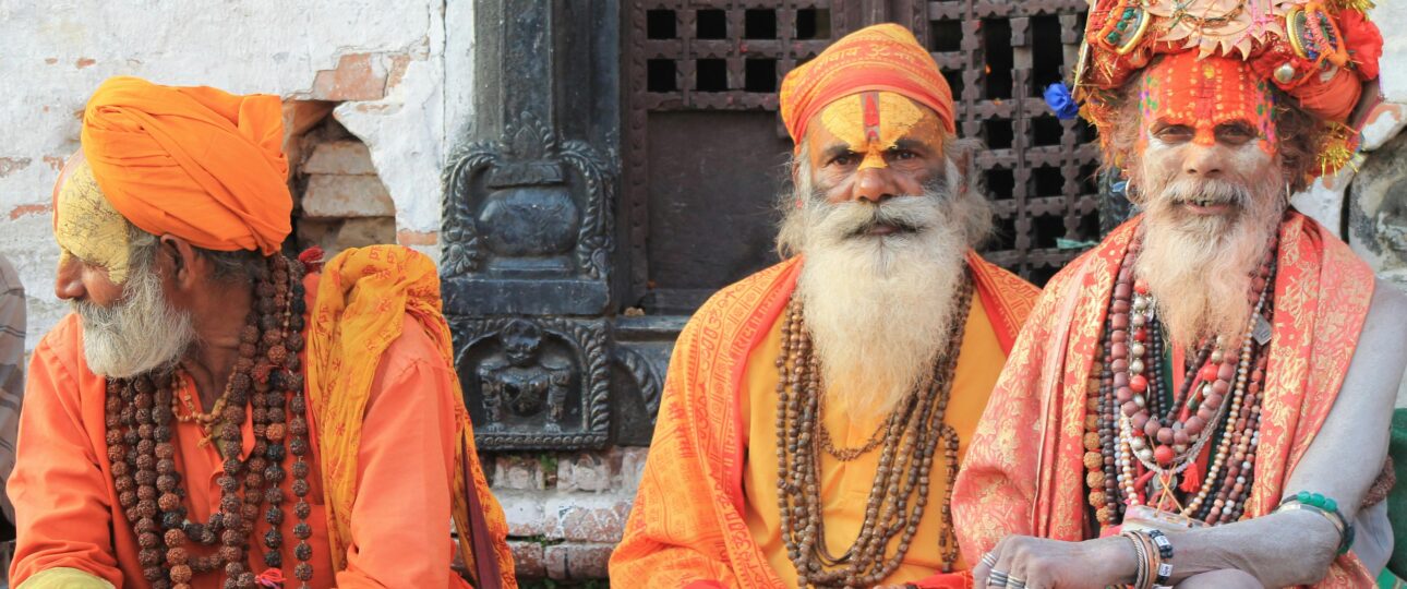 Three sadhus in orange robes with painted faces at Pashupatinath Temple, Kathmandu, Nepal.
