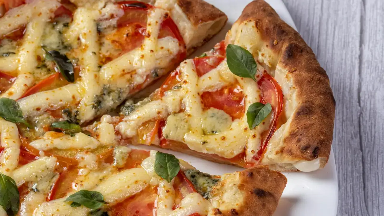 Pizza de tomate e queijo com folhas de manjericão frescas sobre uma base dourada e crocante, com uma fatia já retirada e uma camada de queijo derretido visível.
