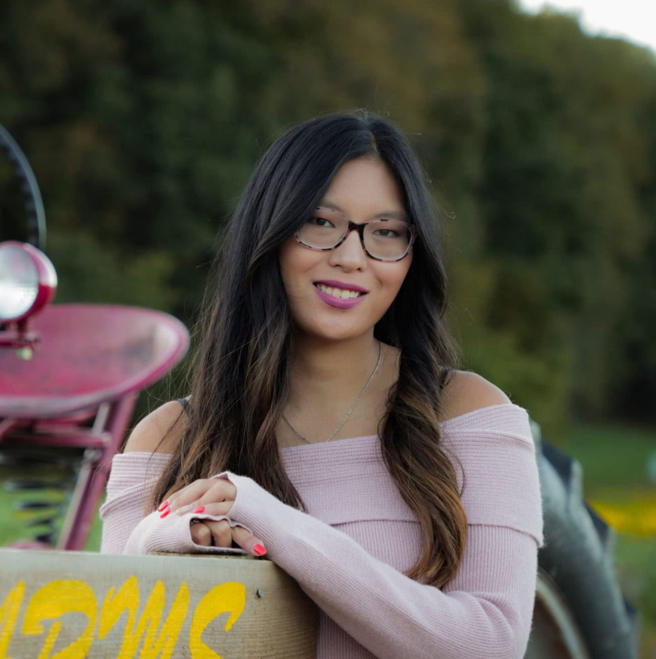 Vintage pink tractor at 407 and Beyond Vacation Co. with a cheerful woman enjoying farm life.