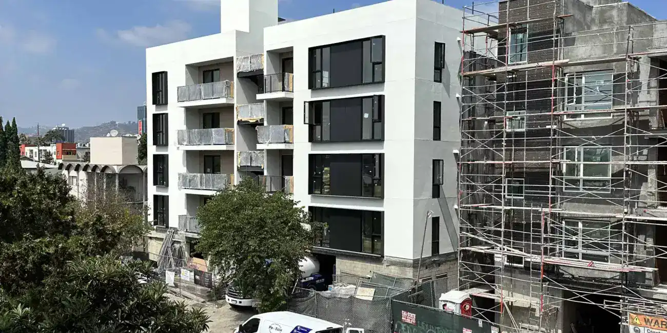 Contemporary white apartment building with large black framed windows and open balconies, modern minimalist style, under construction.